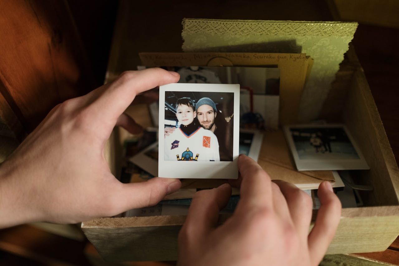 Close-up of hands holding a nostalgic Polaroid photo of father and son from a memory box.